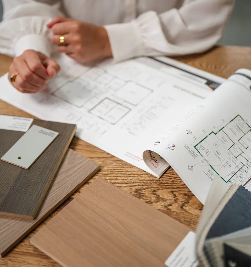 Printed Fowler Homes floor plans spread on a table with timber and fabric samples